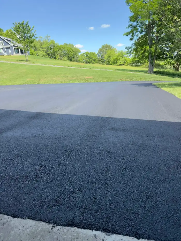 Freshly laid asphalt driveway, the new mat still dark against the compacted surface beyond