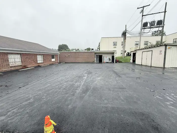 Freshly resurfaced service yard between a brick building and a larger block, wet from rain