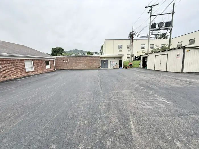 Resurfaced service yard on a dry day, with a wooded ridge rising behind the buildings