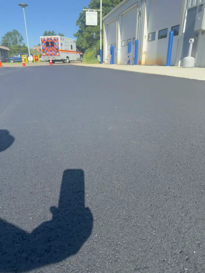 Newly paved apron outside an emergency services station, with an ambulance parked beyond the bay doors