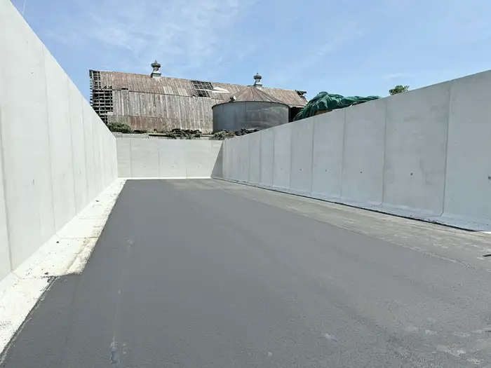 New asphalt laid between poured concrete walls on a farm, with a timber barn and grain bin behind