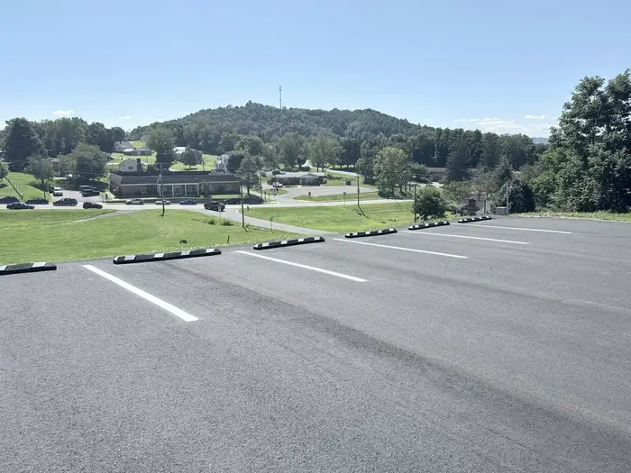 Freshly striped hilltop parking lot with black and white wheel stops, overlooking a town in the valley
