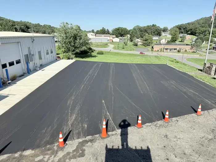 Newly surfaced lot beside a metal building, cones marking the join with the older cracked asphalt