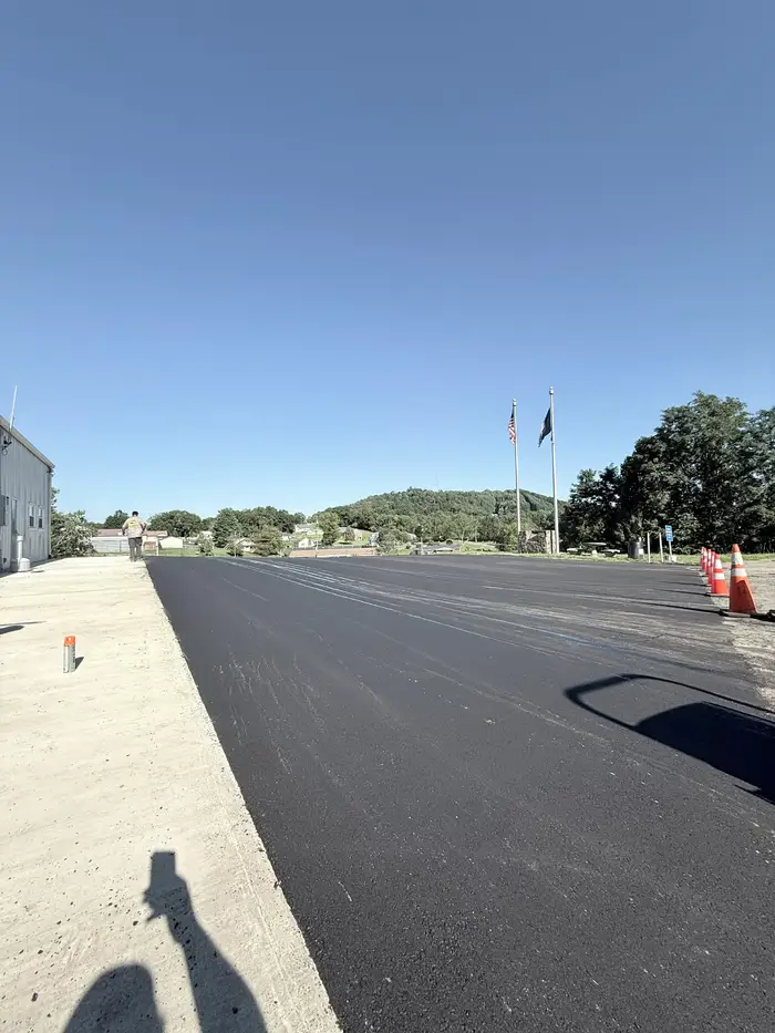 Long strip of fresh asphalt beside a concrete apron, with US and Virginia flags on poles beyond