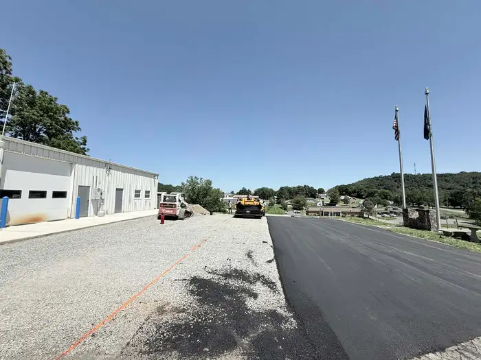 Paver and skid steer at work, prepared stone base on one side and finished asphalt on the other