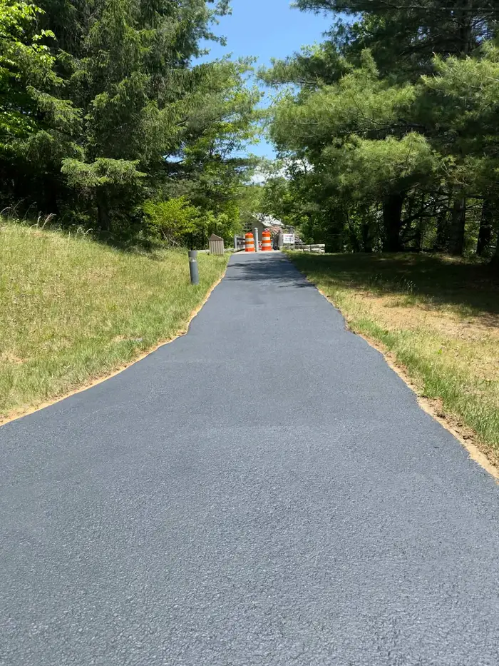 Long freshly sealed drive climbing between pine trees, closed off with orange barrels