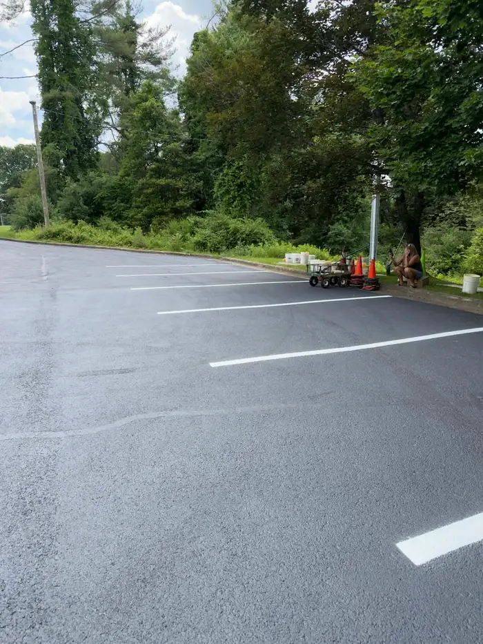 Freshly sealed and striped lot backing onto woodland, with a striping cart, cones and sealer pails