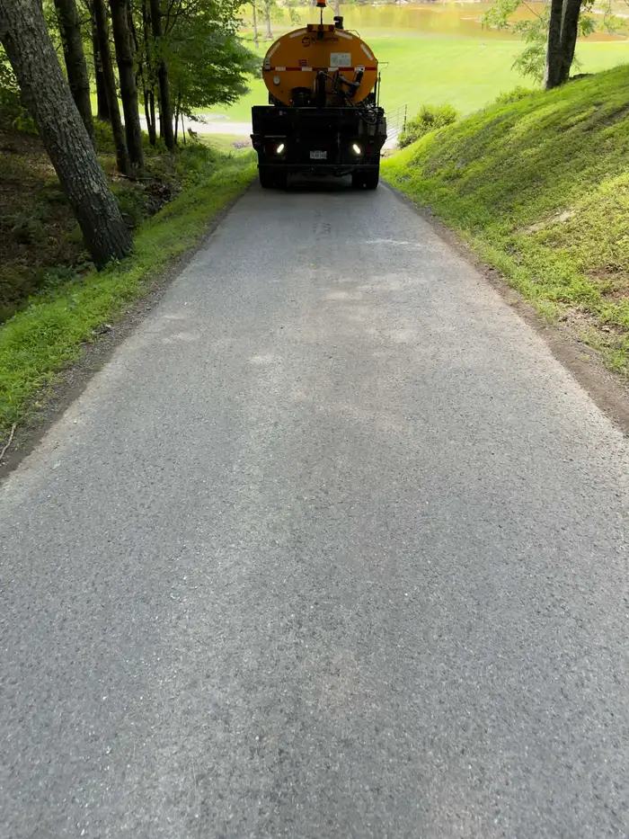 Yellow distributor truck at the head of a freshly chipped driveway running downhill between wooded banks