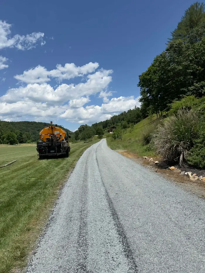 Distributor truck parked on the verge while tar and chip is laid on a long rural drive