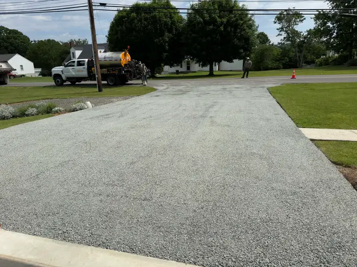 Newly laid tar and chip driveway running down to a village street, distributor truck and crew at the road