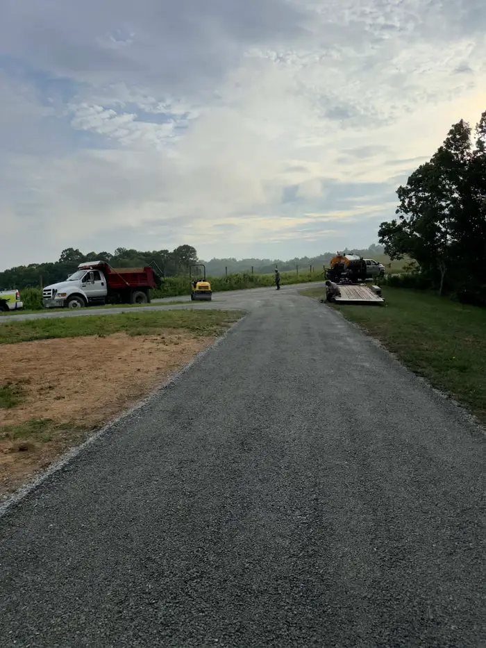 Freshly chipped drive running out to a rural road, with a dump truck, roller and distributor truck on site