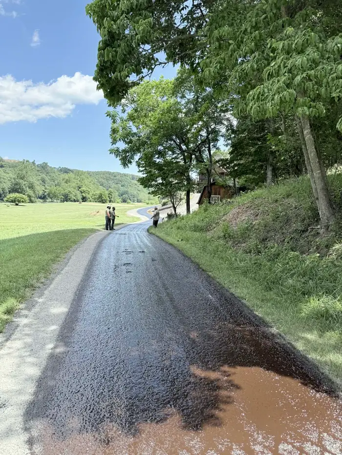 Freshly sprayed asphalt binder covering a private lane before the stone goes down, crew standing further up