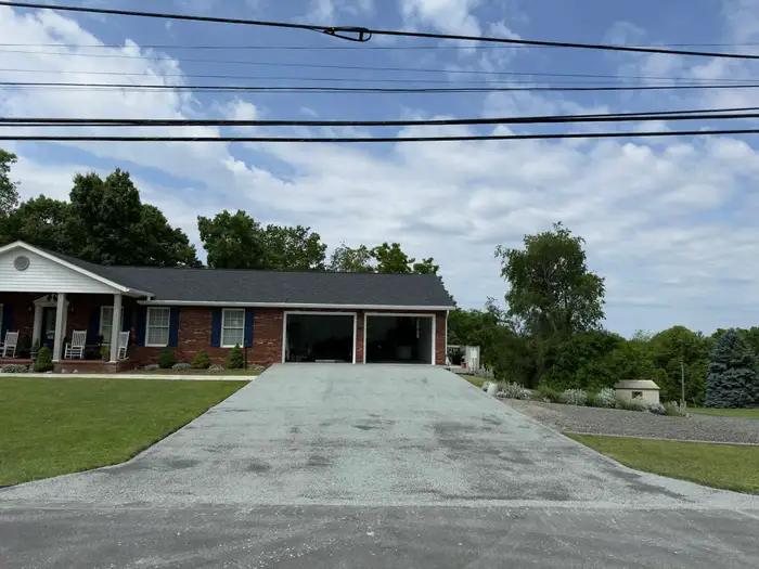 Wide tar and chip driveway running from the street to a two bay garage at a brick ranch house