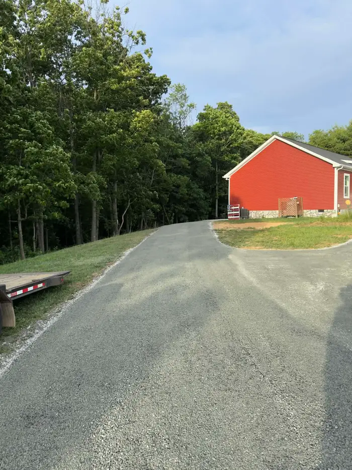 Tar and chip driveway opening into a turnaround beside a red house, woodland along one side