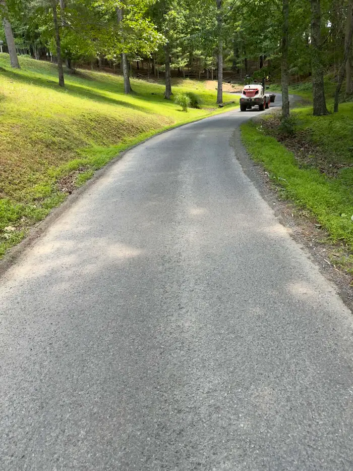 Long chip sealed lane curving through mown wooded grounds, with a roller parked further up
